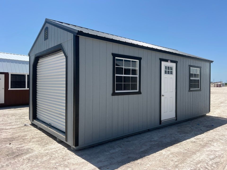 Gray shed with a roll-up garage door, white door, windows, and black trim.