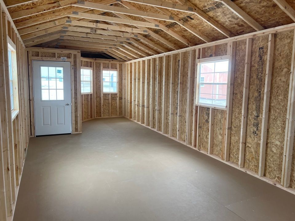 Interior view of a wooden shed under construction with a door, windows, and exposed studs.