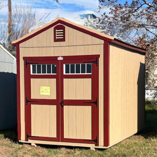 Tan shed with maroon trim and double doors. Set on grass, with a small vent near the peak of the roof.