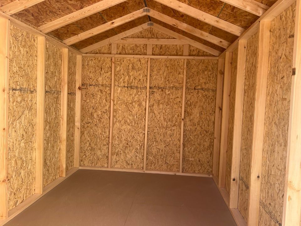 Interior view of an empty wooden shed with OSB walls, floor, and a pitched roof.
