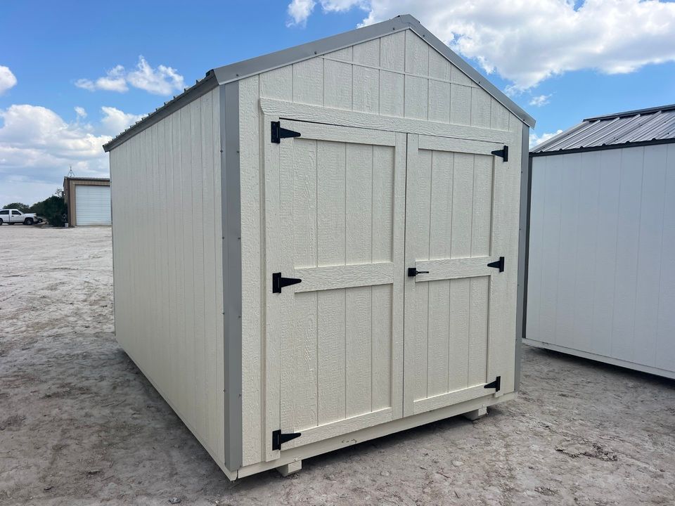 Tan storage shed with double doors, gray trim, and roof, set outdoors on a sunny day.