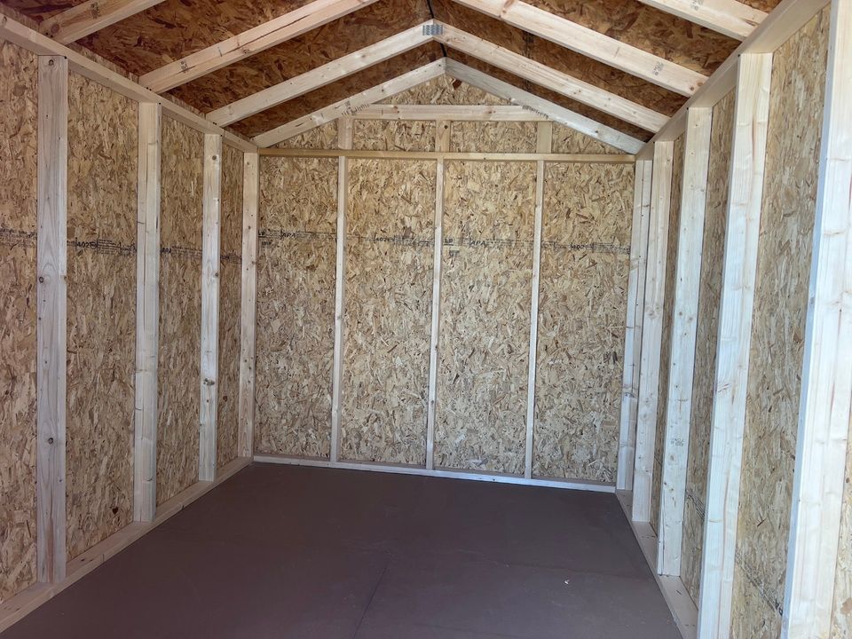 Interior view of an empty shed with a brown floor and wood-paneled walls and ceiling.