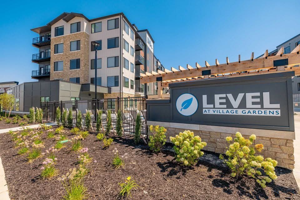 Level at Village Gardens sign in front of a multi-story apartment building under a blue sky.