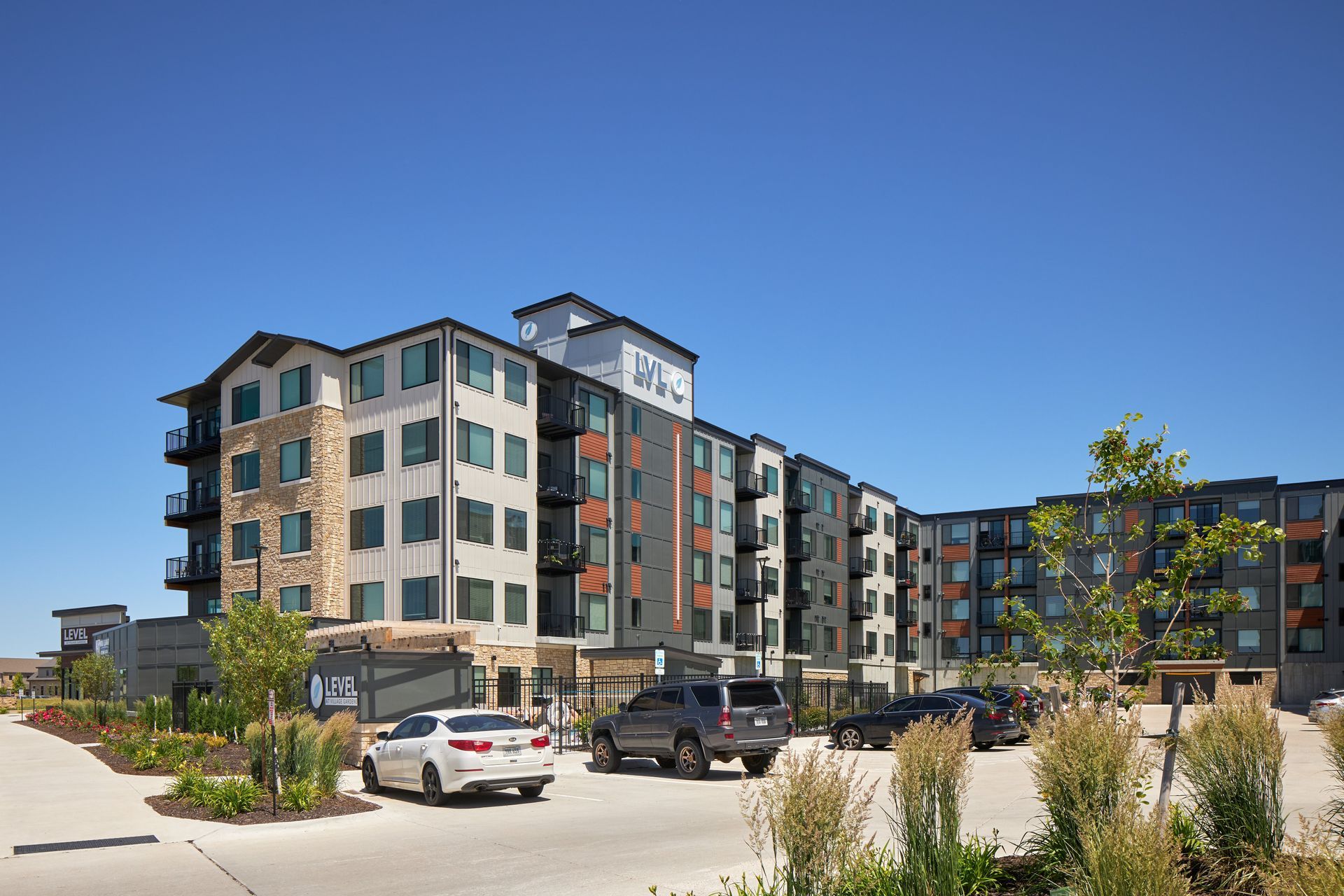 Apartment building with cars parked out front, under a clear blue sky.