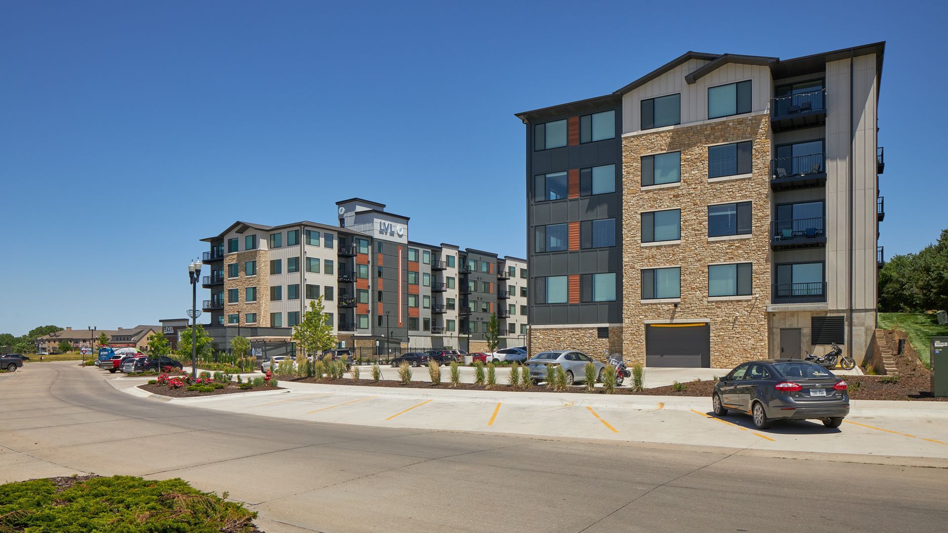 Modern apartment buildings with varied facade textures and colors, parked cars, and clear sky.