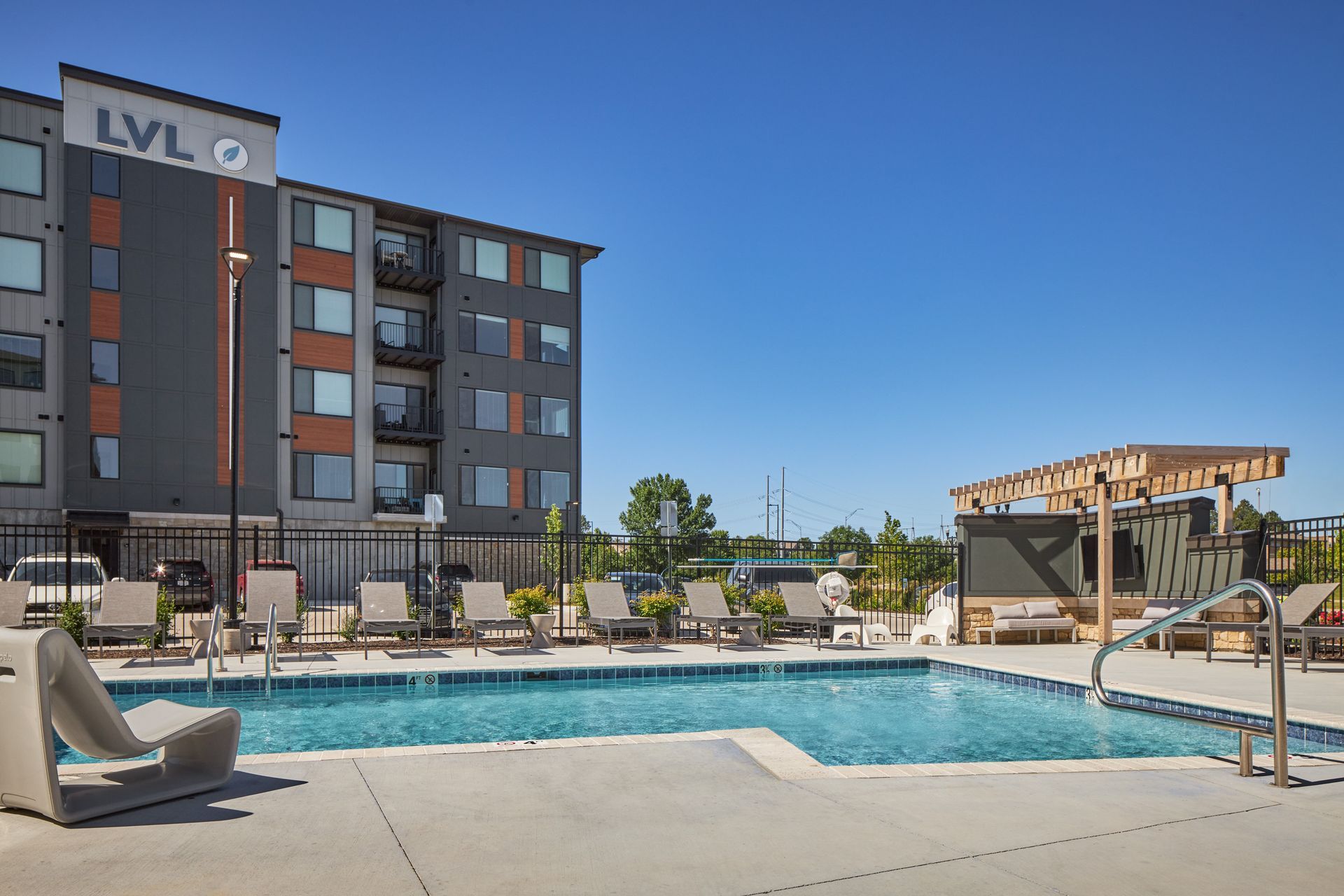 Pool area with lounge chairs, next to an apartment building with 