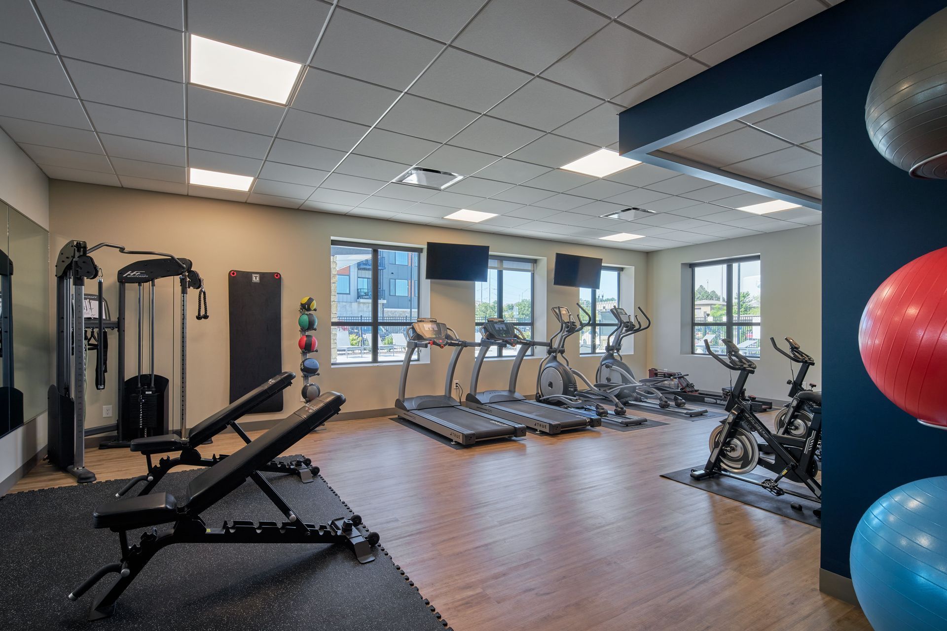 Gym interior with fitness equipment: treadmills, weights, stationary bikes, and exercise balls.