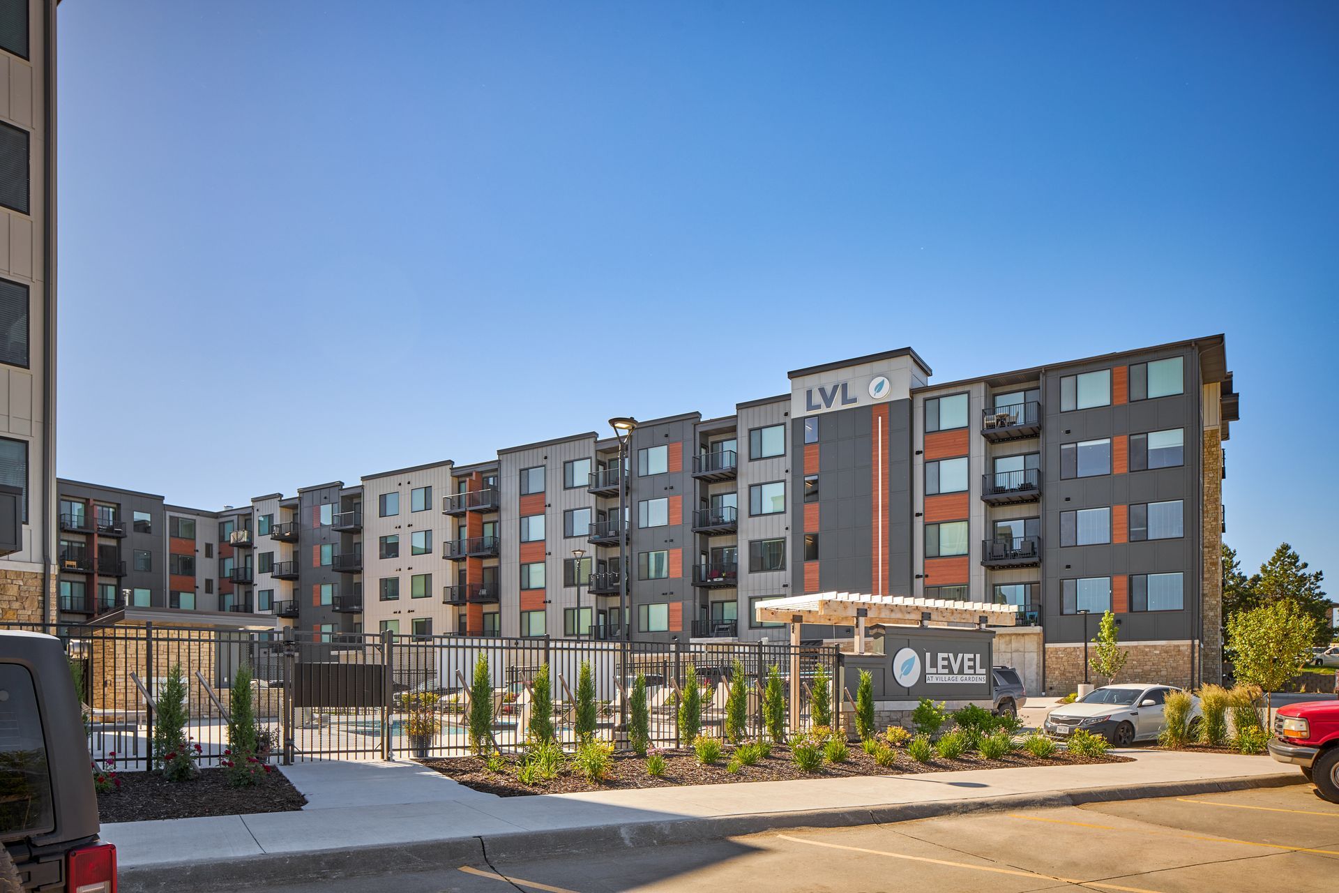 Apartment building with grey facade, LVL logo sign, and cars parked outside under a blue sky.