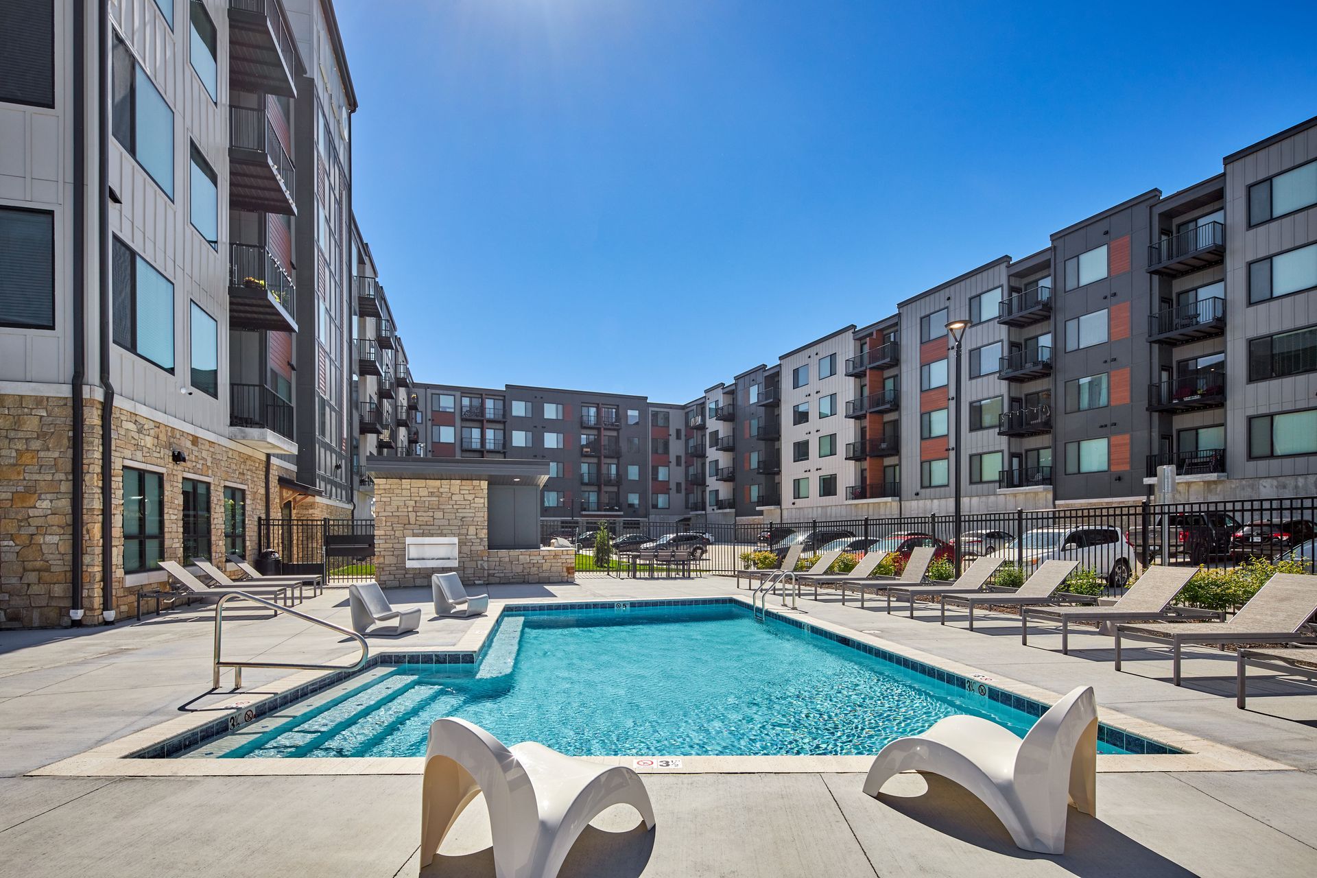 A sunny courtyard with a pool, lounge chairs, and apartment buildings.