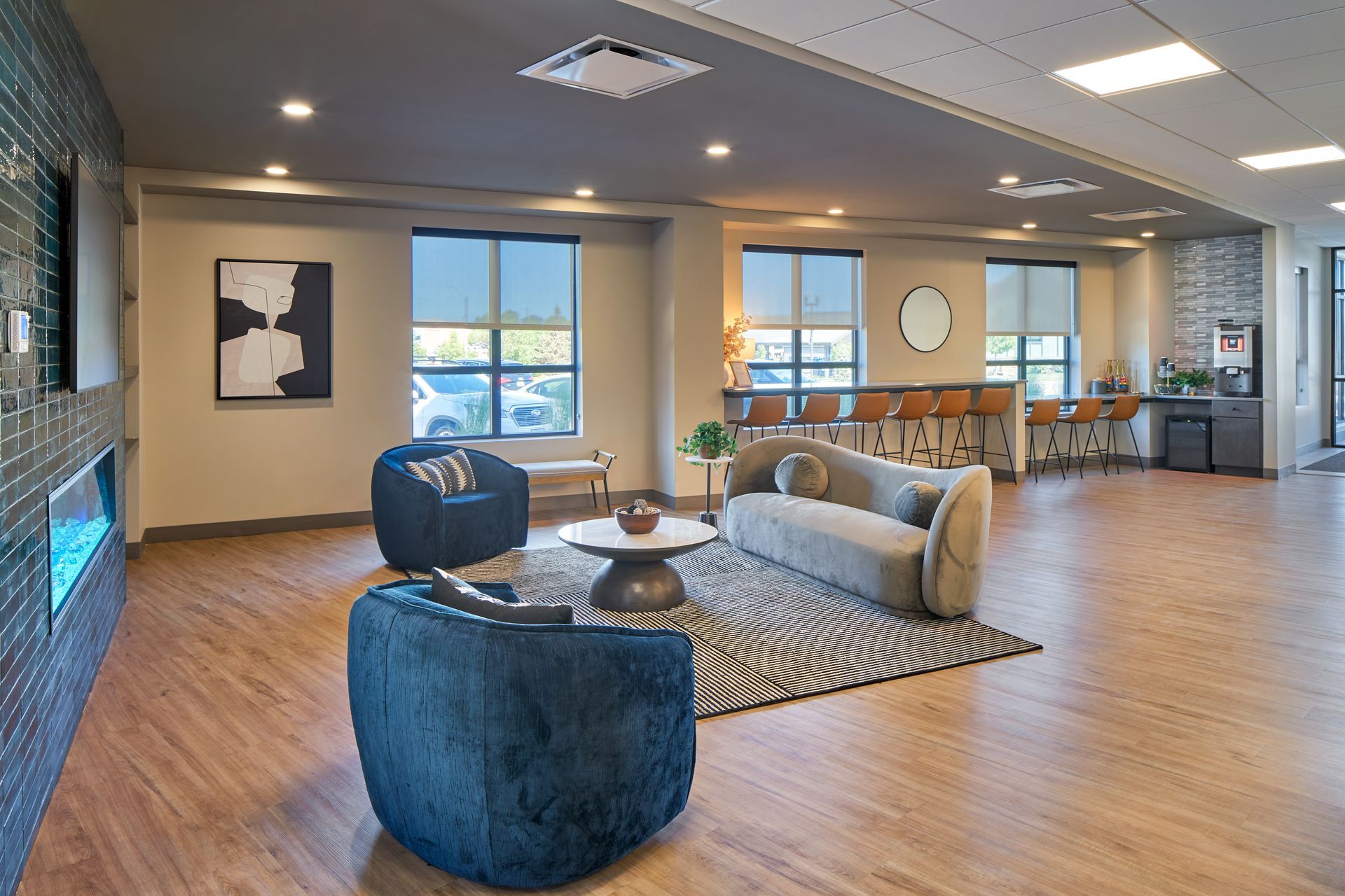 Lounge area with blue chairs, a sofa, and a rug. Windows and a bar area are visible.