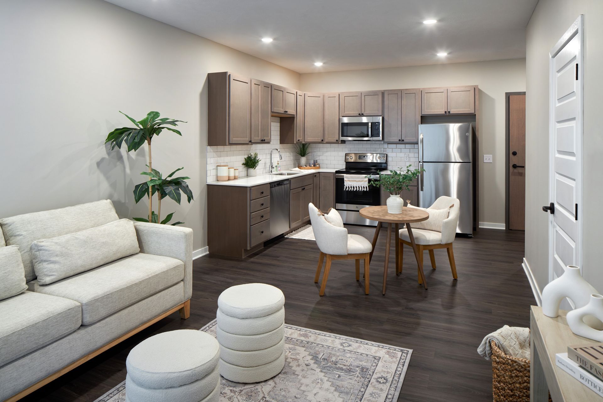 Modern apartment interior: kitchen with stainless steel appliances, dining area, and living room with sofa.