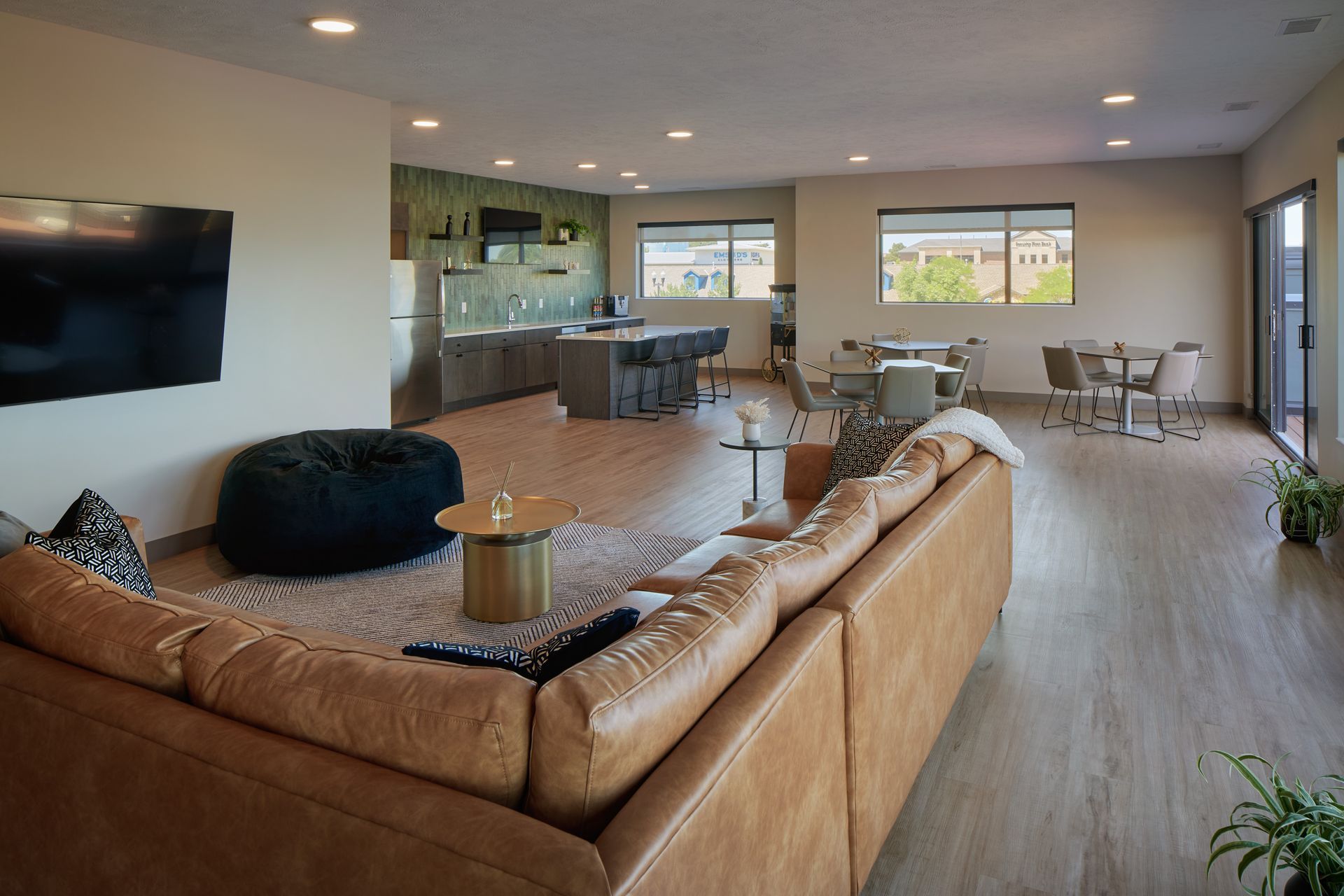 Spacious living area with kitchen, dining set, and large brown leather couch on wooden floor.