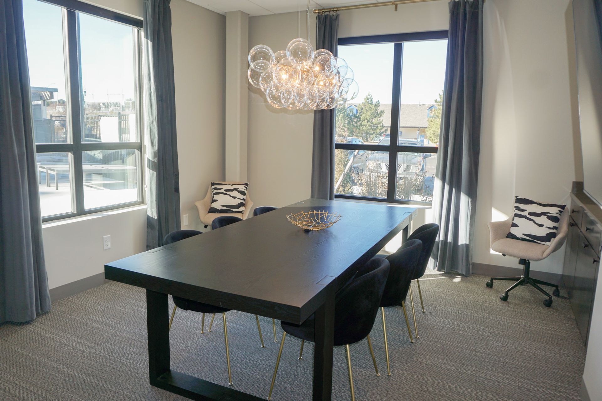 Dining room with large rectangular table, six black velvet chairs, a bubble chandelier, and large windows with gray curtains.