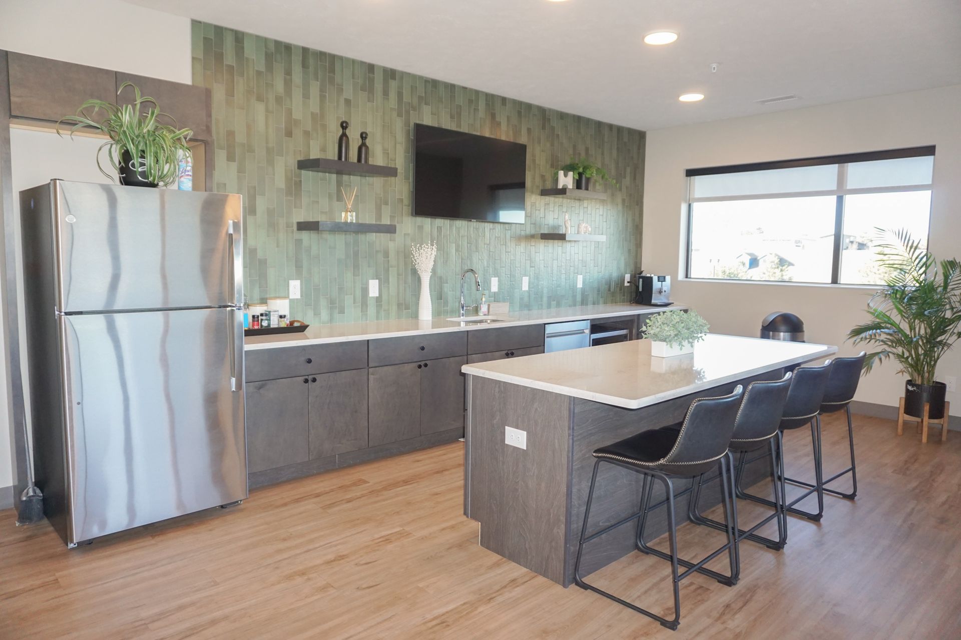 Modern kitchen area with stainless steel fridge, island with seating, and green accent wall with TV.