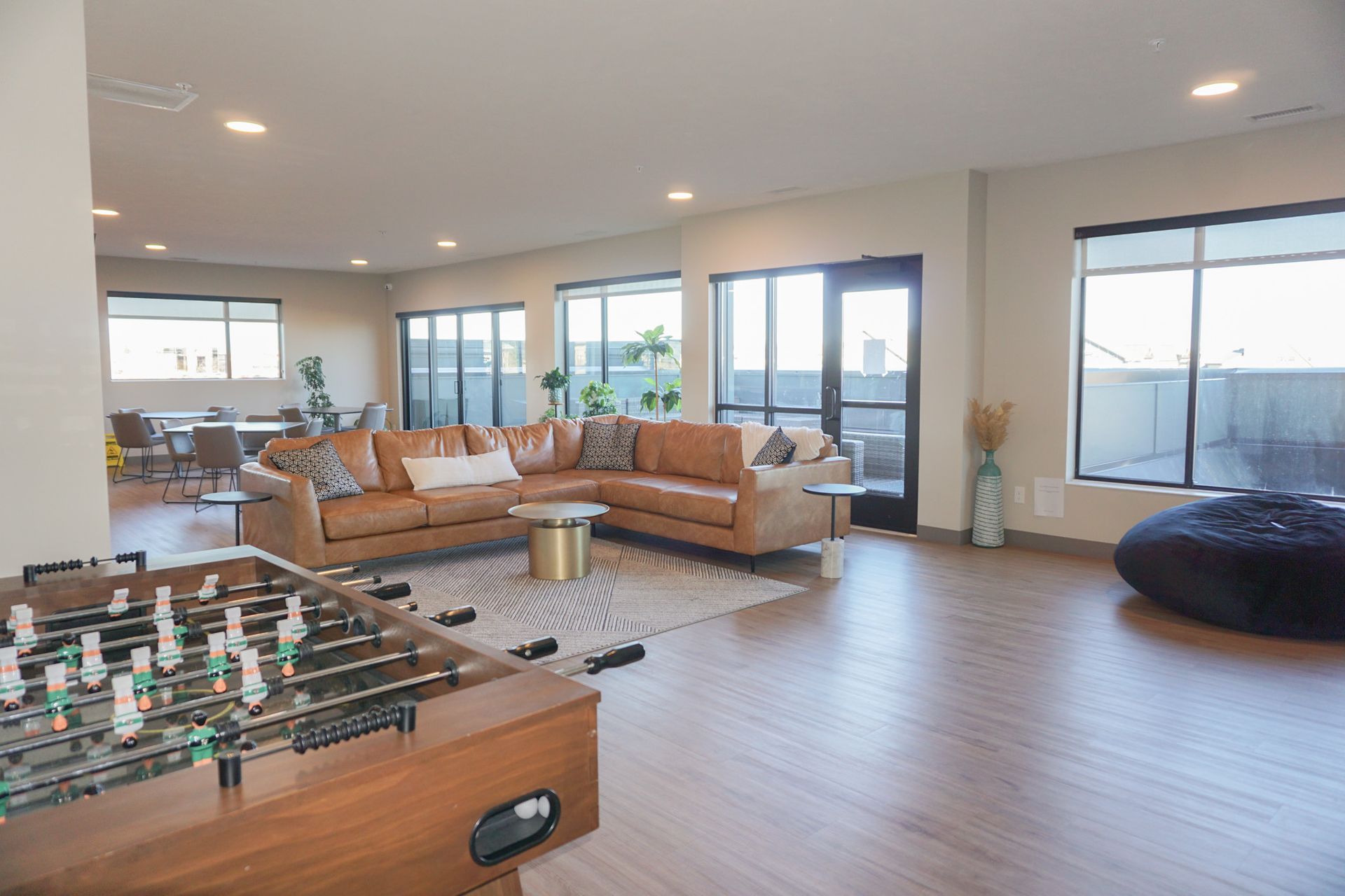 Spacious lounge area with foosball table, brown leather sectional, large windows, and beanbag chair.