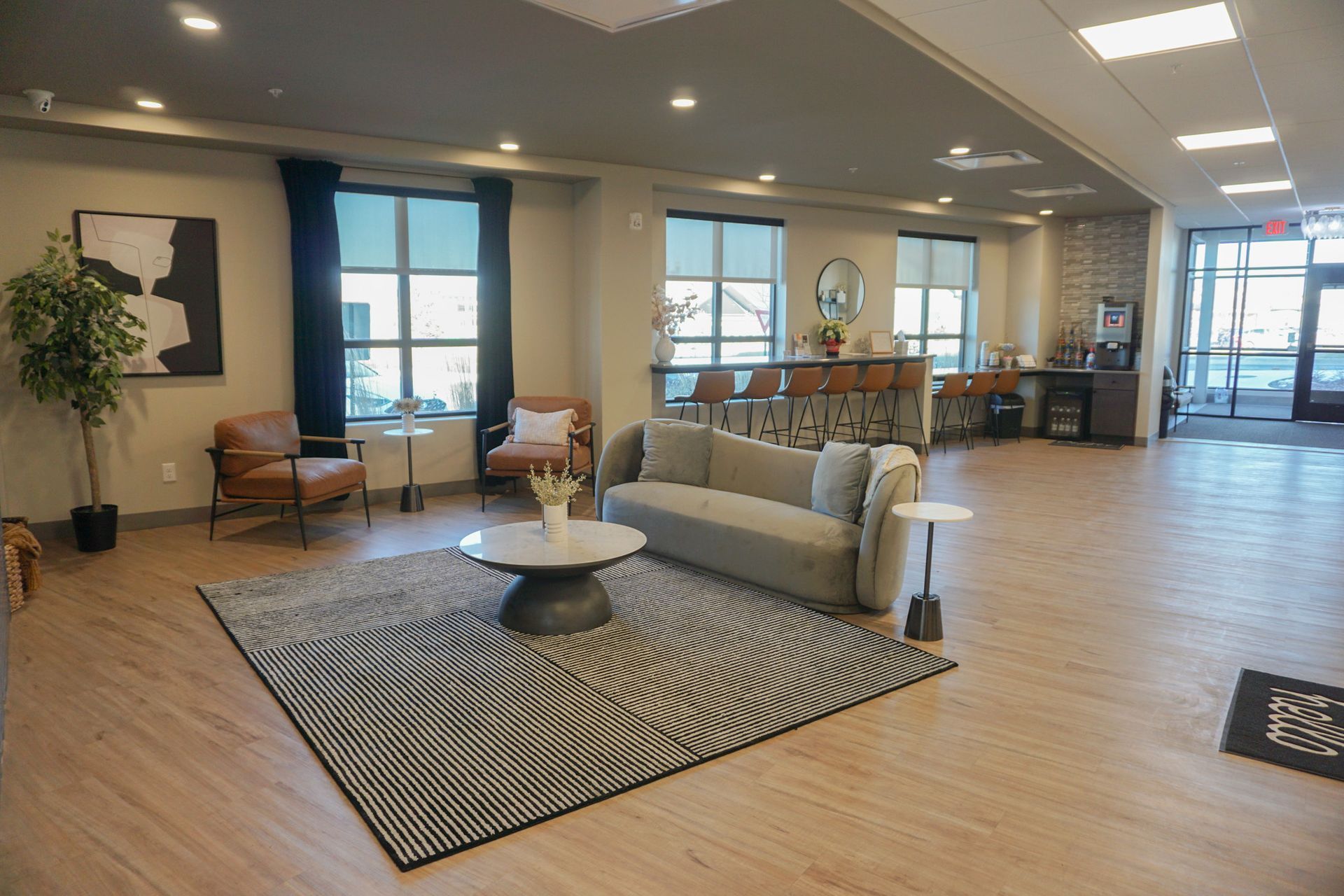 Lounge area with light wood floors, a rug, sofa, chairs, bar, and large windows.