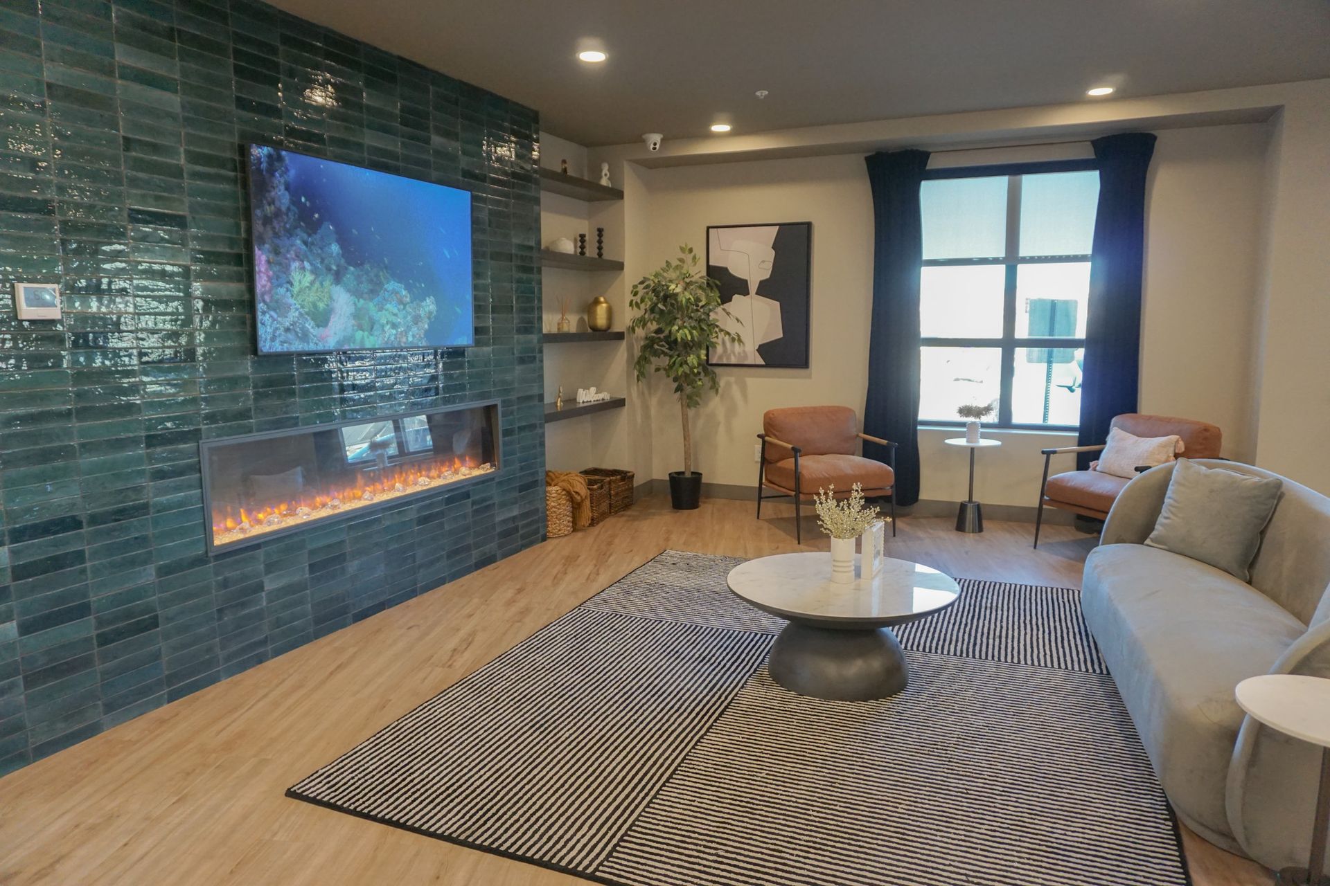 Living room with teal tiled fireplace, TV, seating area, rug, and window.