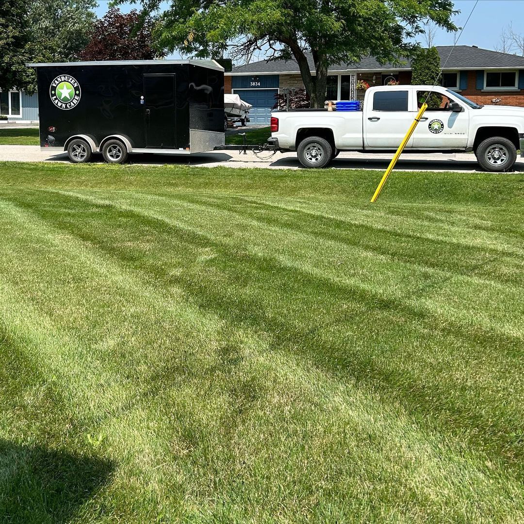 A white truck is parked next to a black trailer in a lush green field.