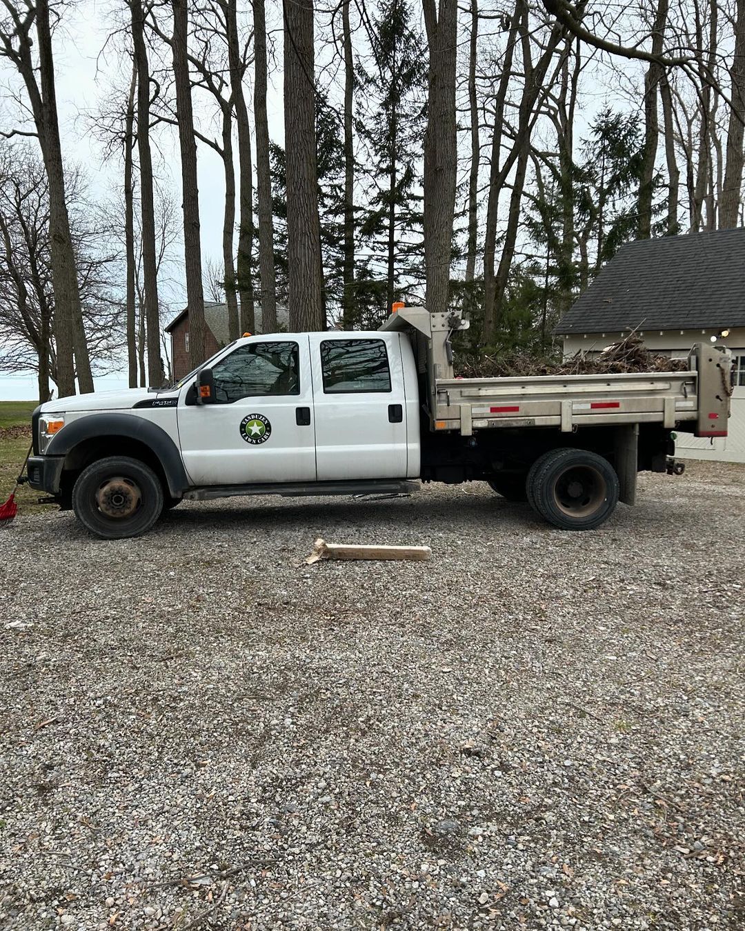 A white dump truck is parked in a gravel lot in front of a house.