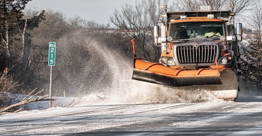 A snow plow is driving down a snowy road.