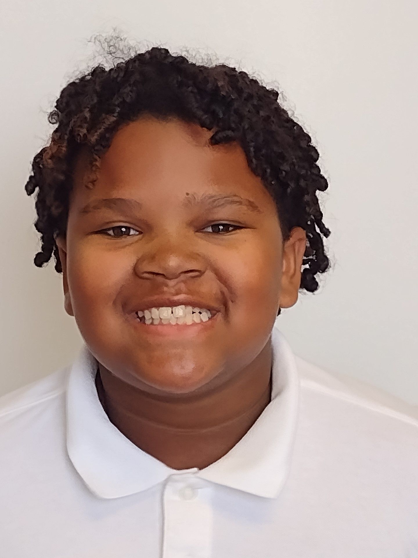 A young boy wearing a white shirt is smiling for the camera