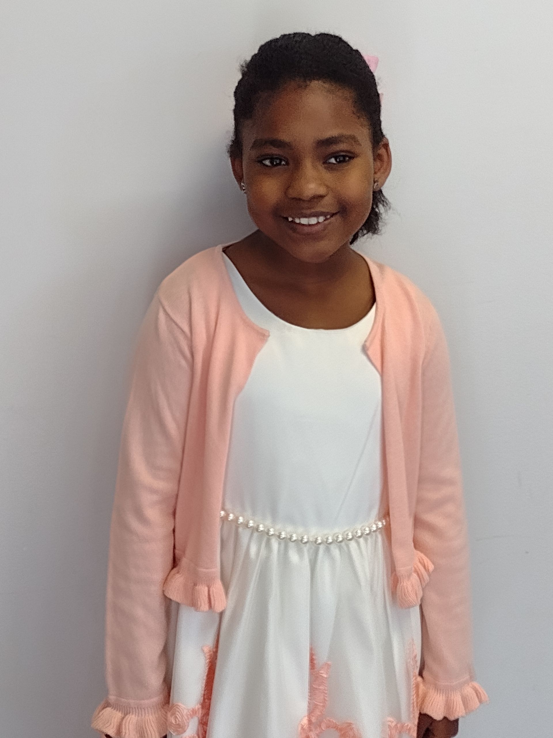 A little girl wearing a white dress and a pink cardigan