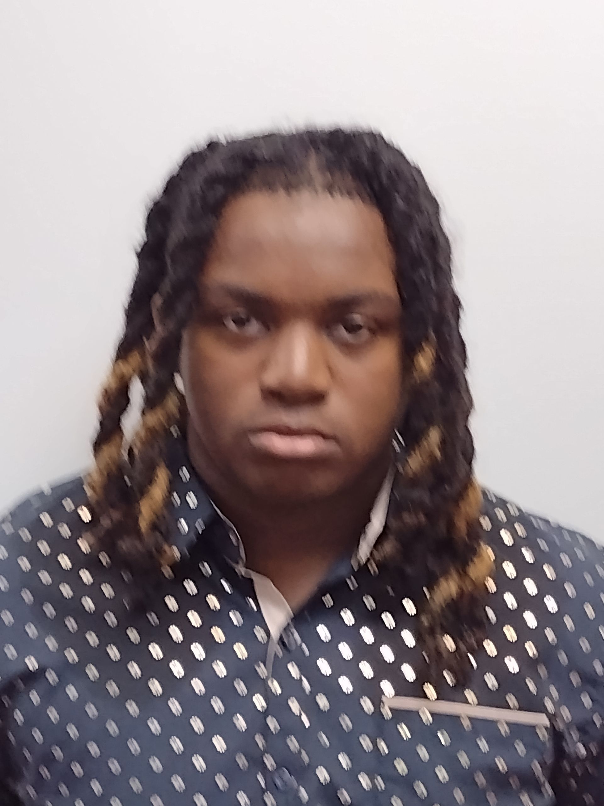 A man with dreadlocks is wearing a polka dot shirt