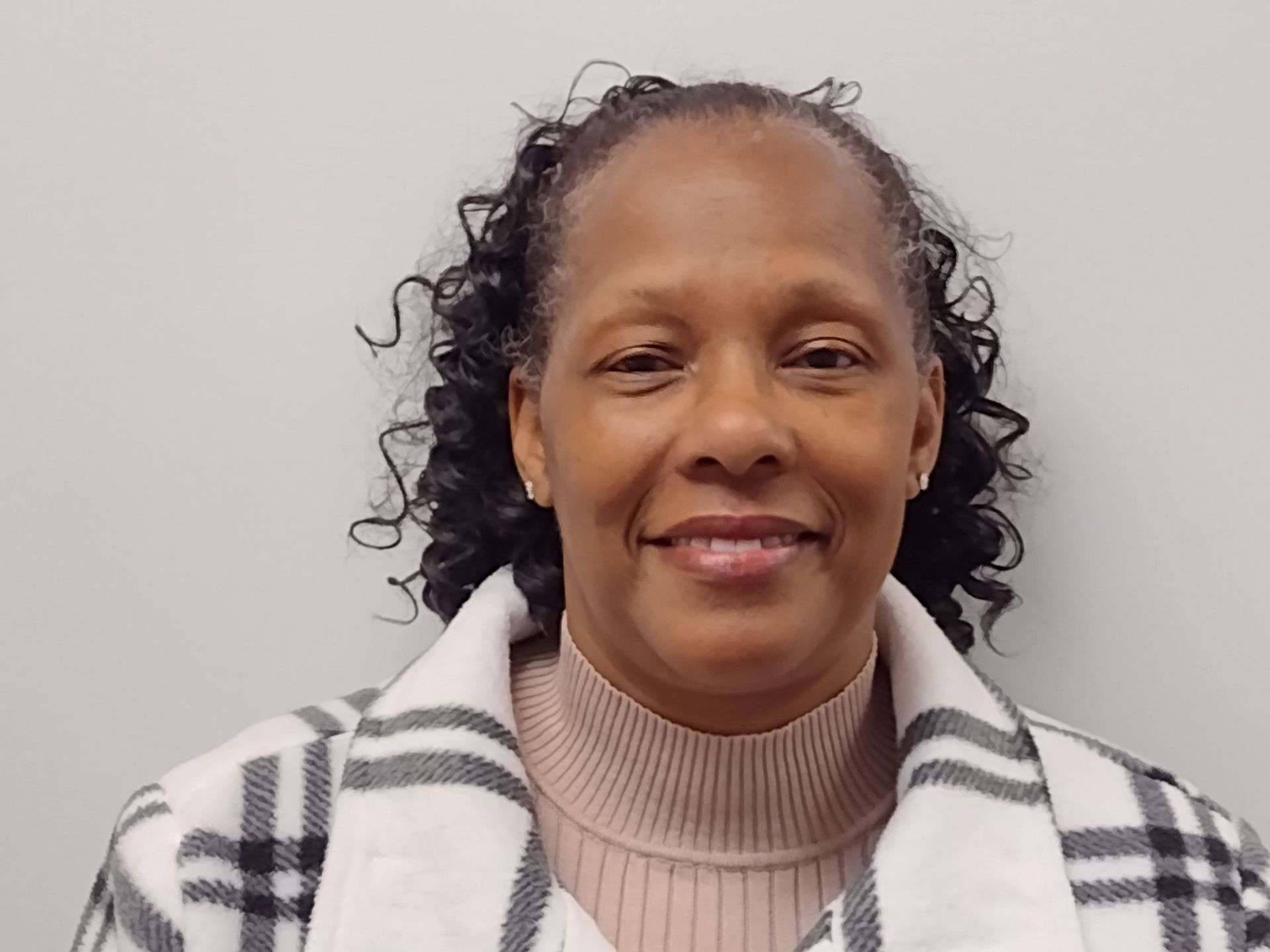 A woman with curly hair is smiling for the camera while wearing a plaid jacket.