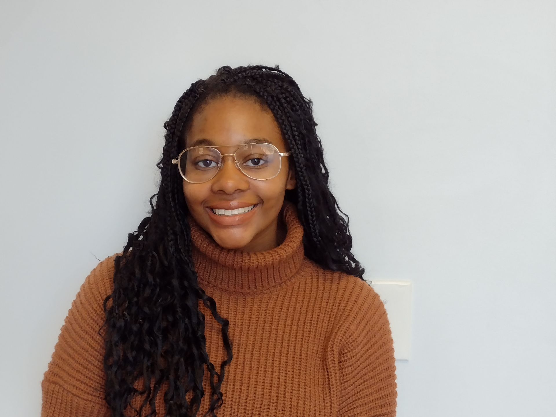 A woman wearing glasses and a brown sweater is smiling for the camera.