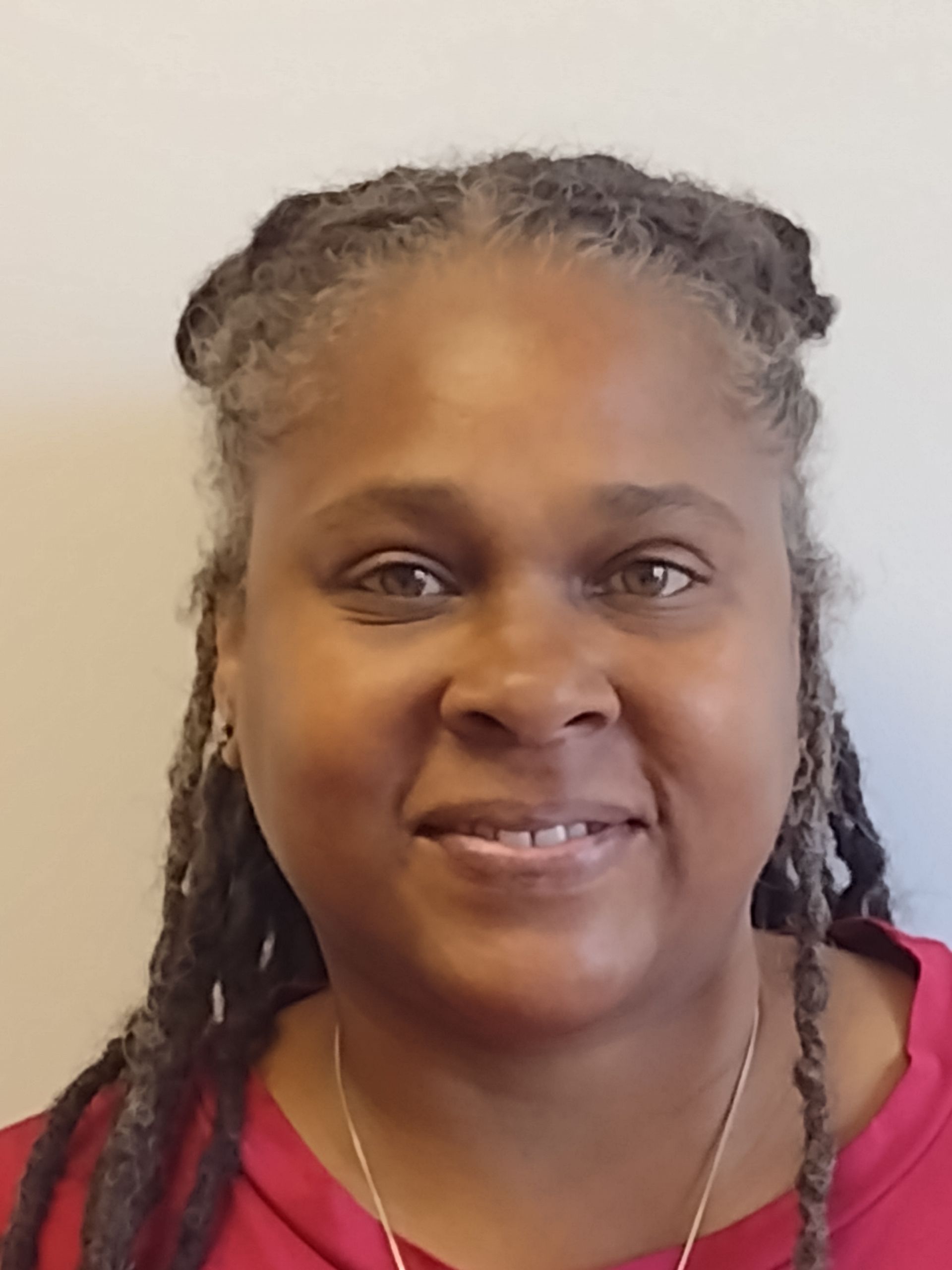 A woman with dreadlocks and a red shirt is smiling for the camera.