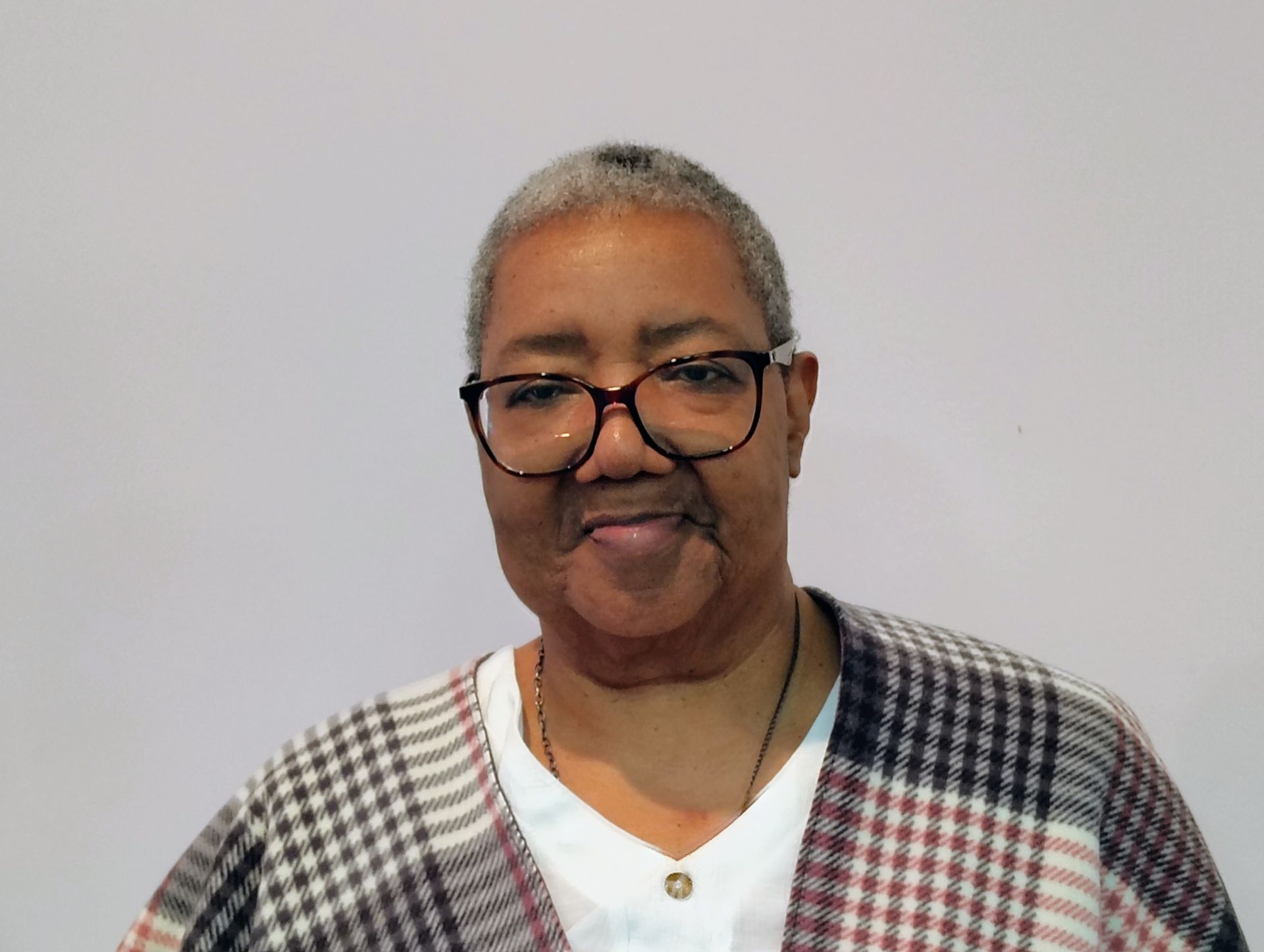 Woman with glasses, short gray hair, wearing a plaid poncho over a white shirt.