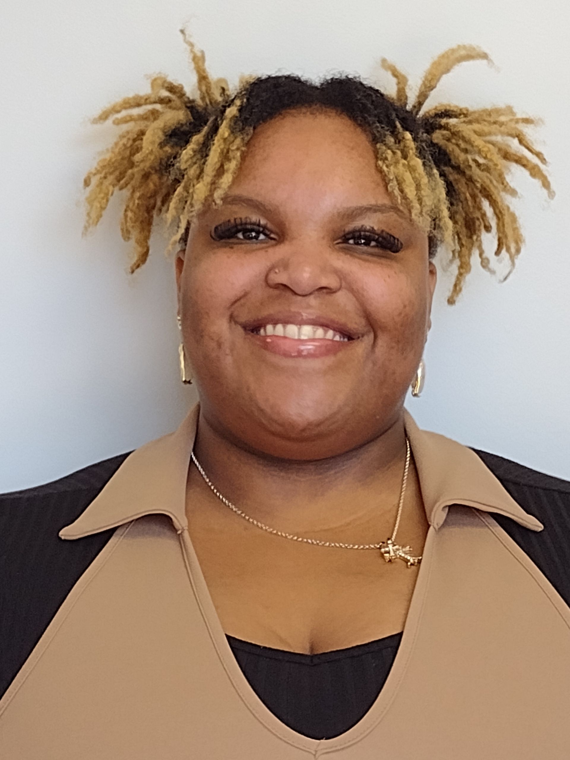 A woman with dreadlocks and a necklace is smiling for the camera.