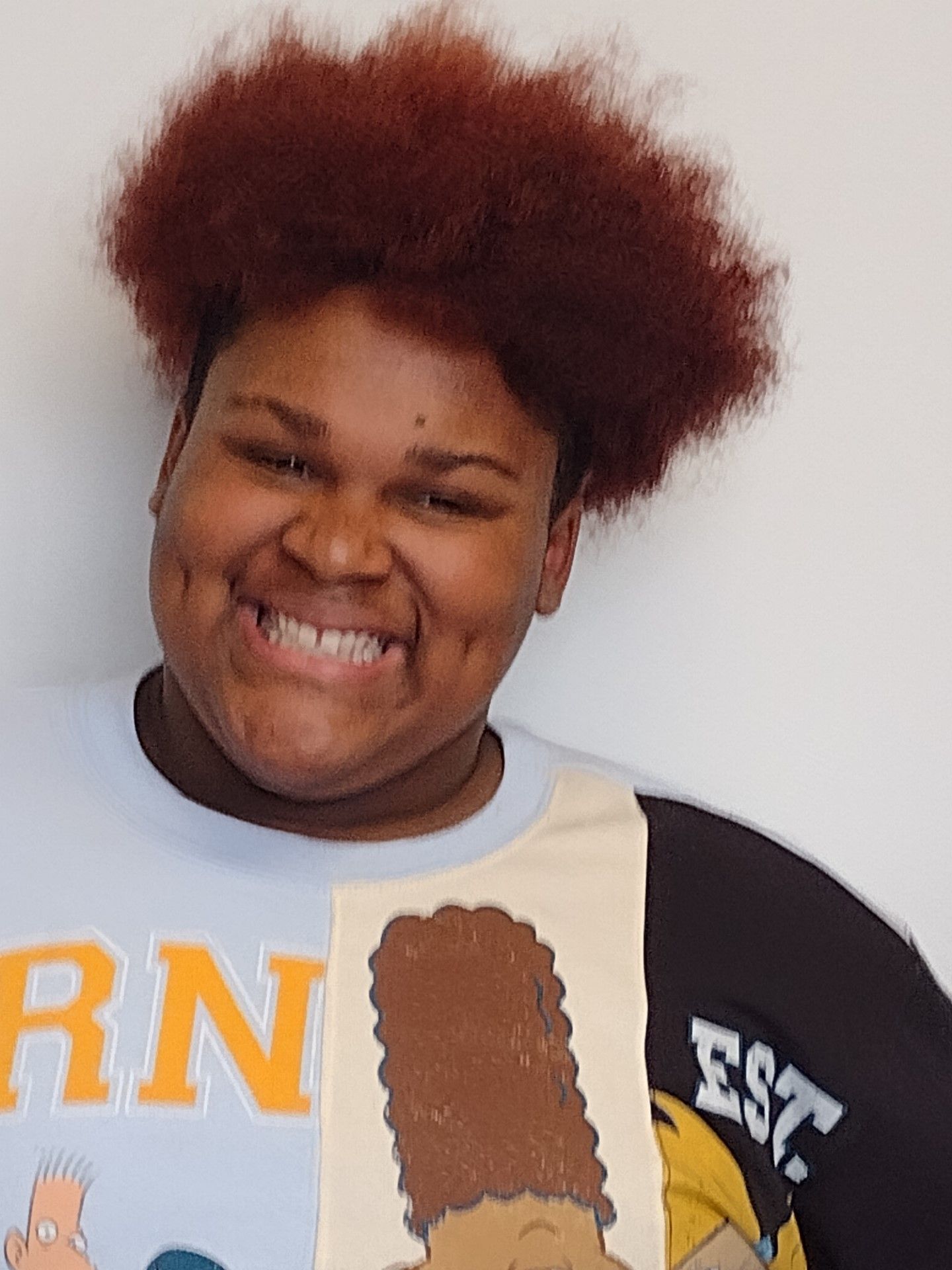 A woman with red hair is smiling and holding a picture of bart simpson