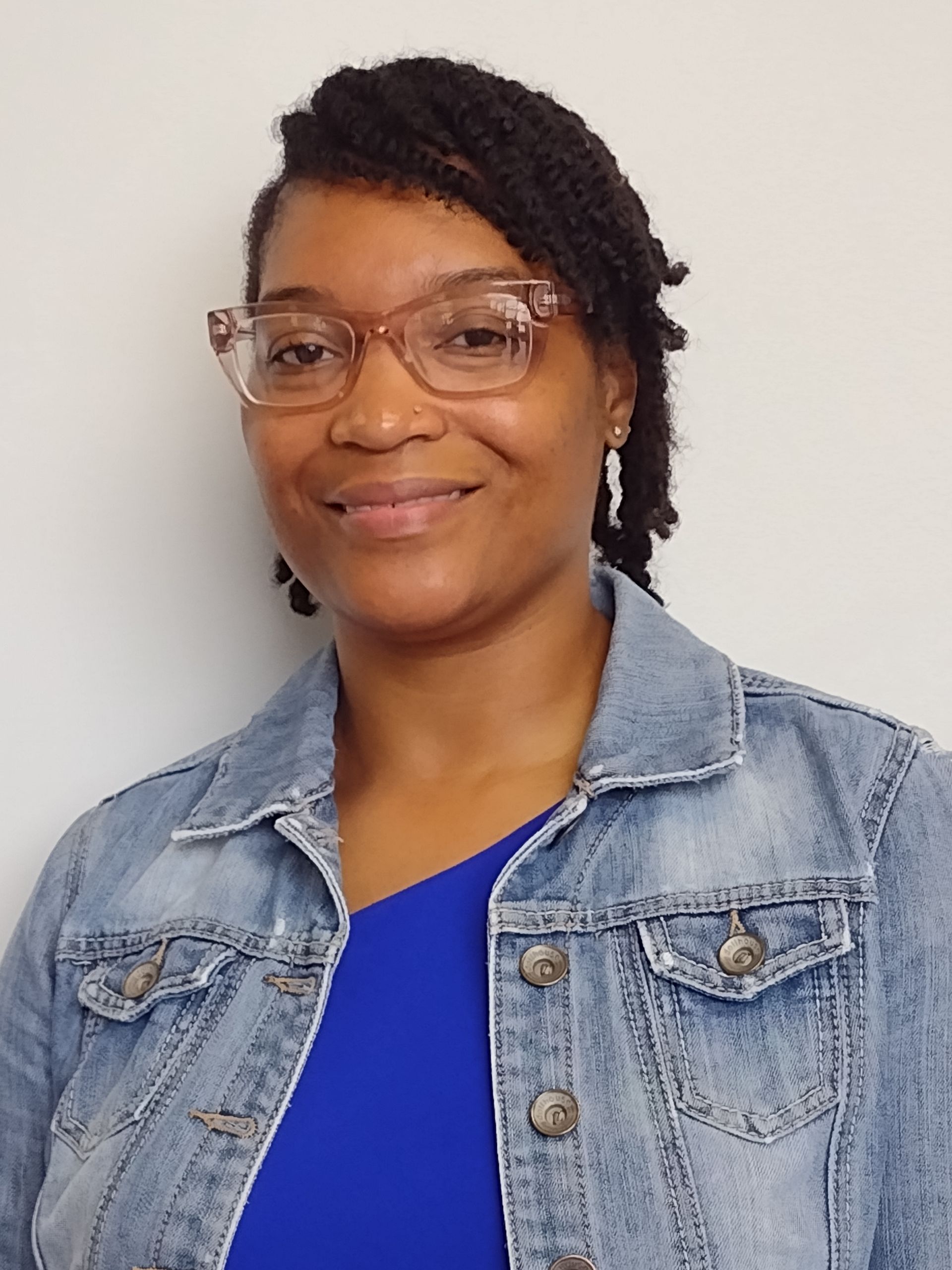 A woman wearing glasses and a denim jacket is smiling for the camera.