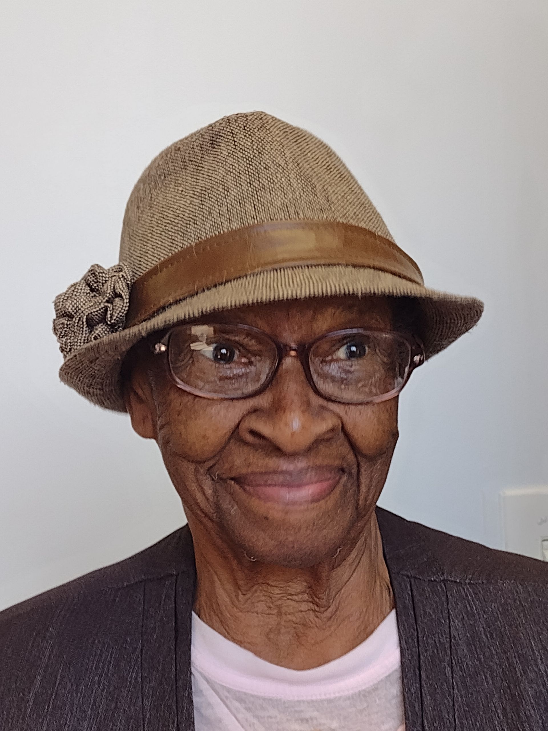 An elderly woman wearing a hat and glasses is smiling for the camera.