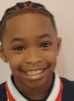 A young boy with braids is smiling for the camera