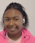 A young girl wearing headphones and a pink jacket is smiling.
