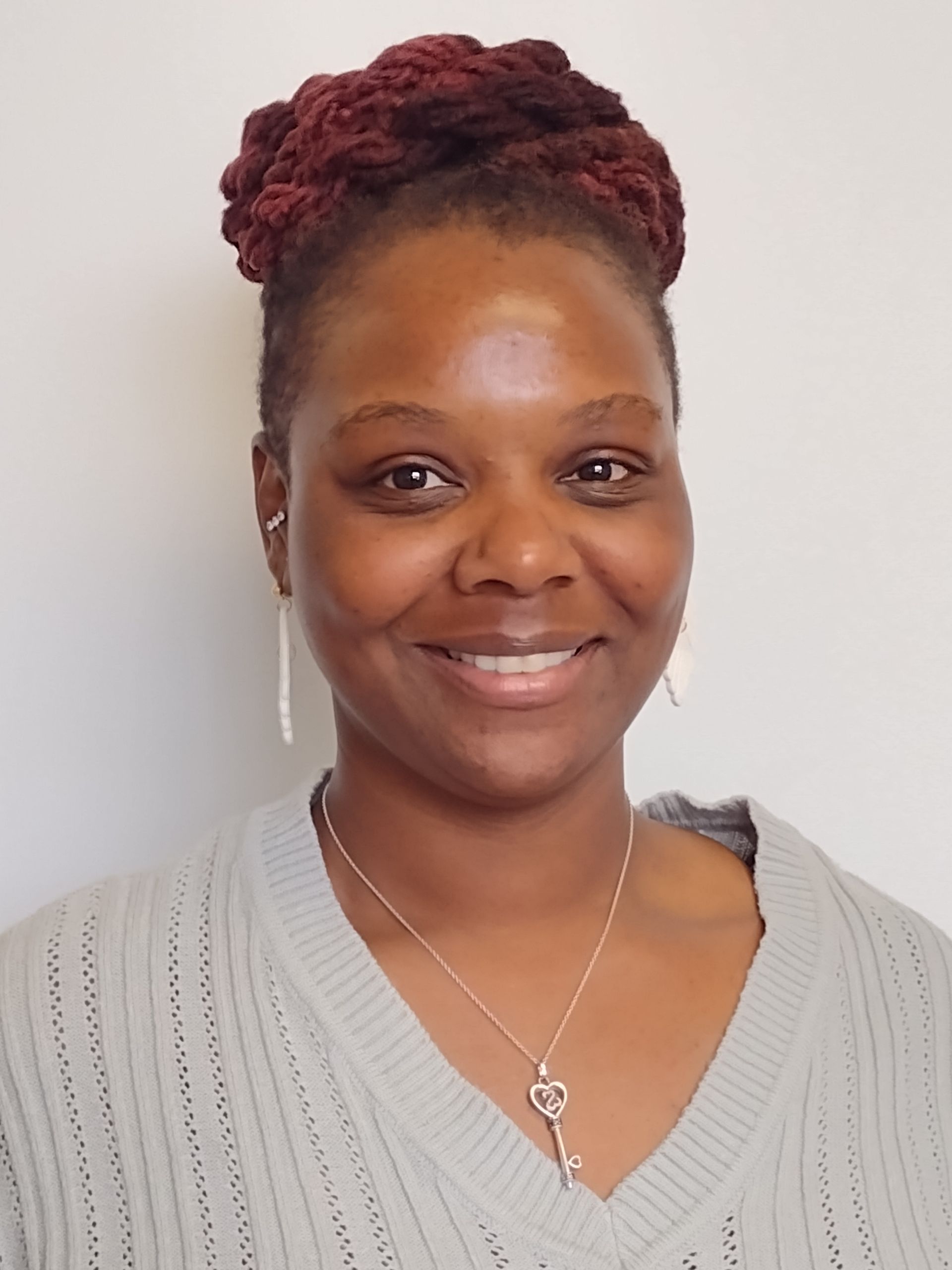 A woman wearing a grey sweater and a key necklace smiles for the camera