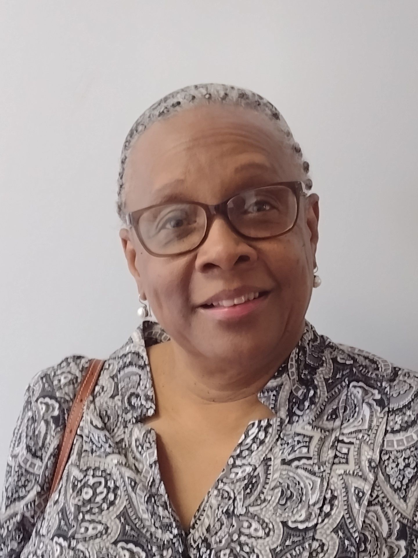A woman wearing glasses and a paisley shirt is smiling for the camera.