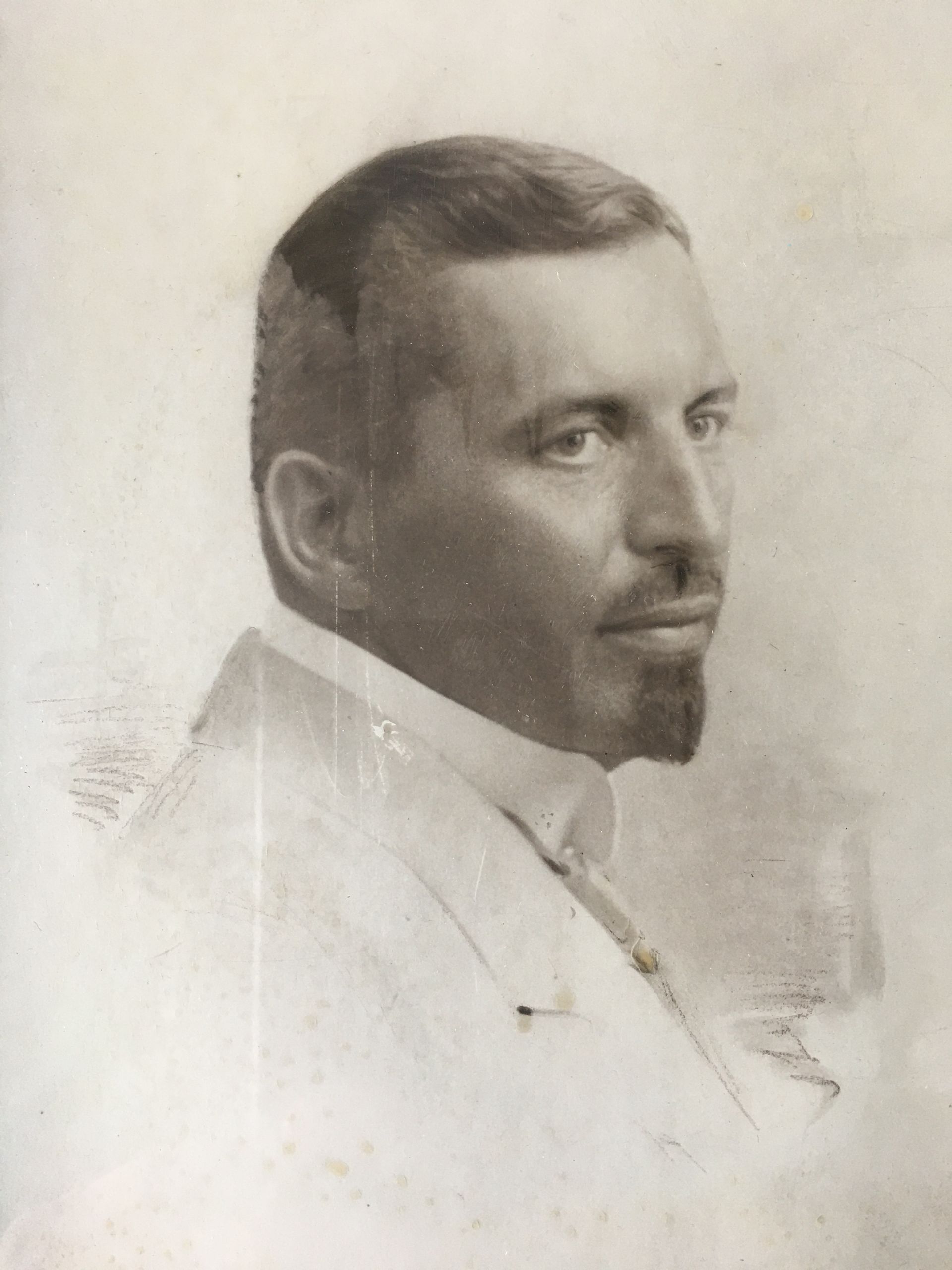 Porträt eines Mannes im weißen Anzug, der mit einem leichten Lächeln zur Seite blickt.