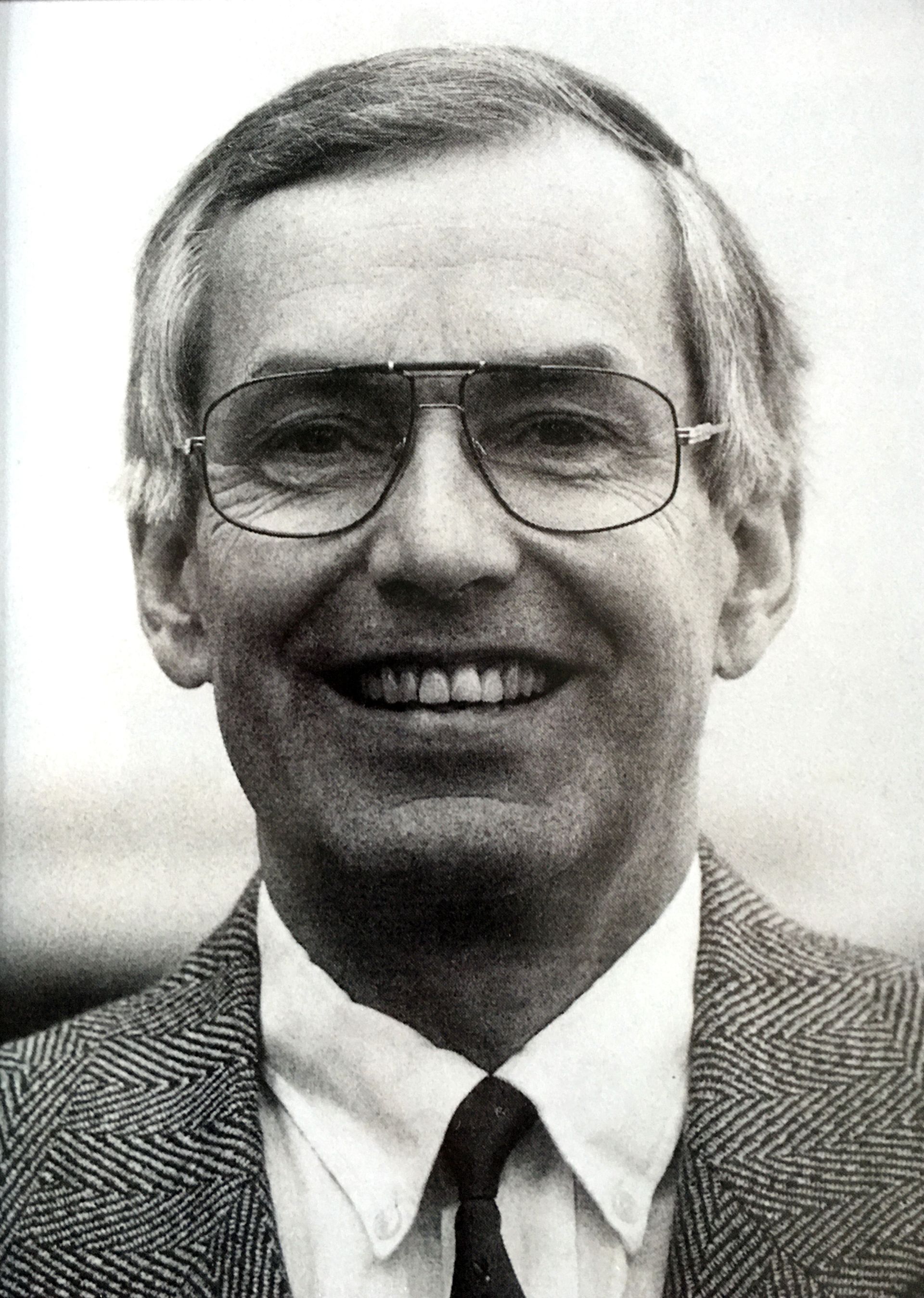 Mann mit Brille, lächelnd, in einem Tweed-Sakko.