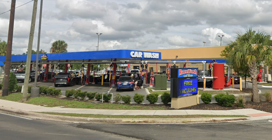 Blue and tan car wash with cars waiting in line; sign reads 