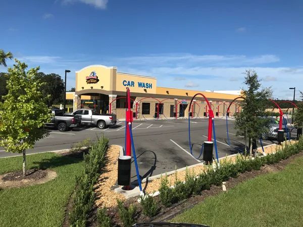 A car wash building with red and blue arches, cars in bays, and a truck parked outside.