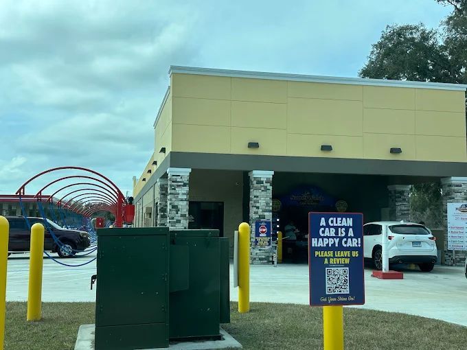 Car wash exterior with entrance arch, sign, and vehicles. Yellow and green building with cars lined up.