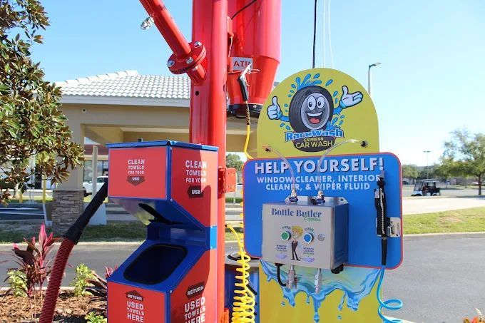 Car wash station with supplies: window cleaner, interior cleaner, and wiper fluid. Red and blue with smiling tire logo.