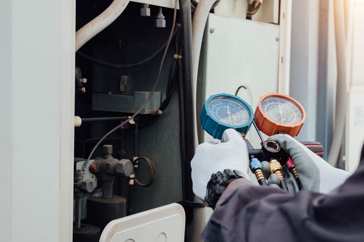 Technician in work gloves using an HVAC manifold gauge set to check refrigerant pressure on an outdoor unit.