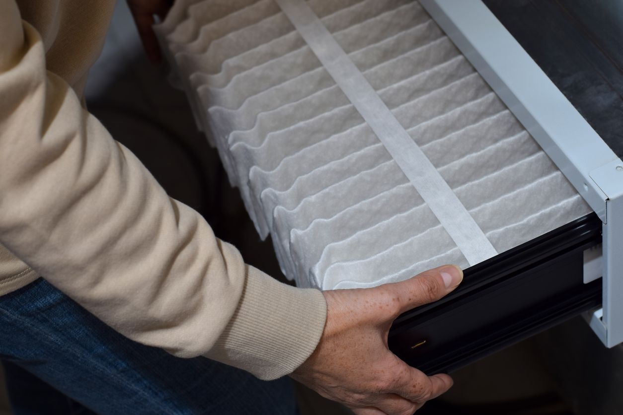 A person slides a white, pleated air filter out of a heating and cooling unit.