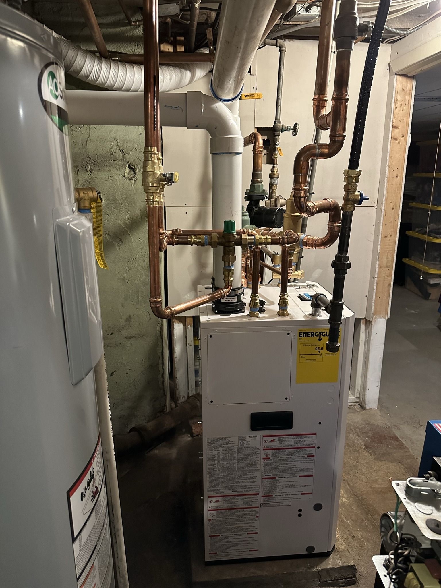 A white furnace and a water heater connected by copper pipes in a utility room.