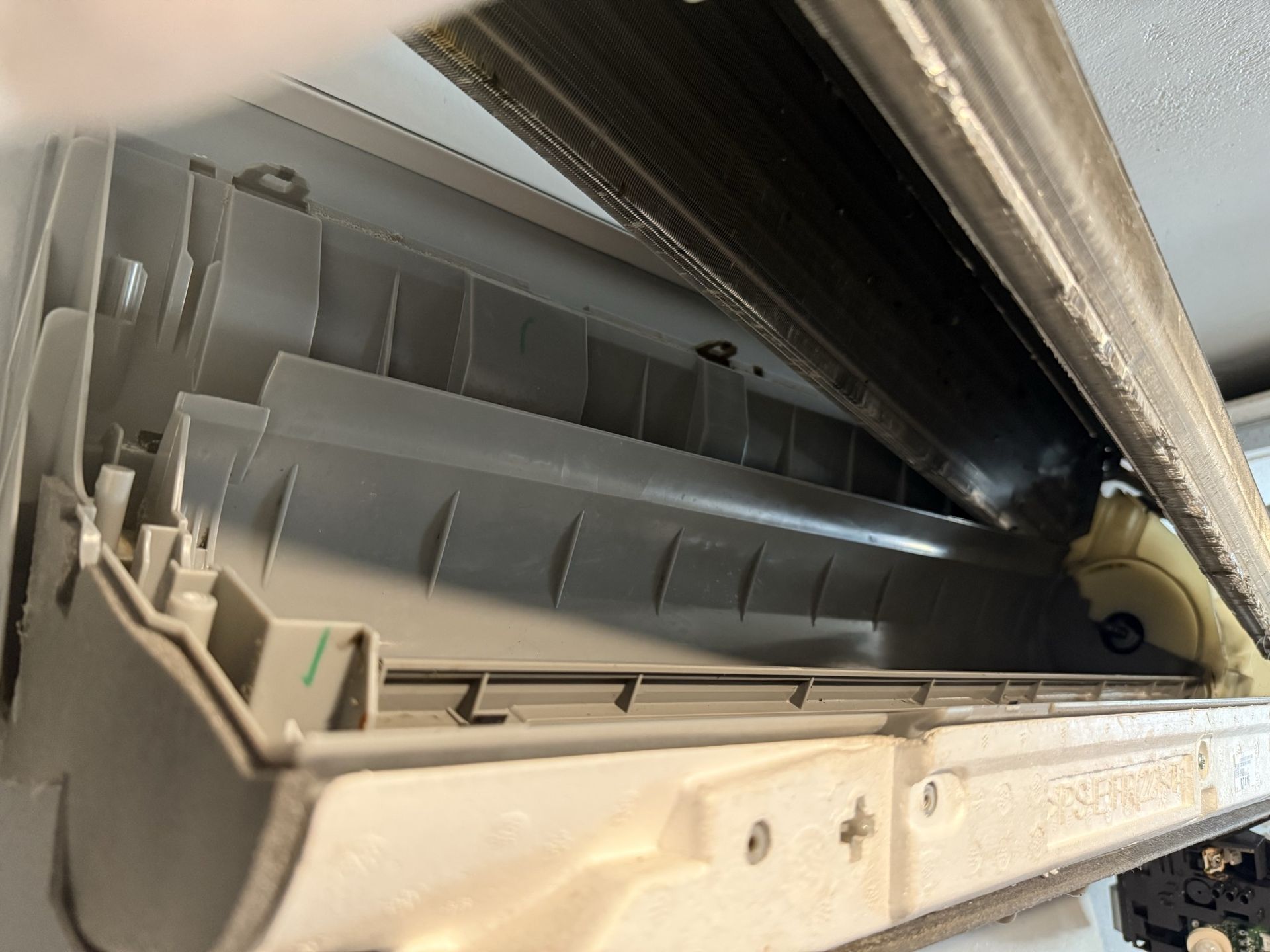 An open, beige indoor air conditioning unit with visible inner cooling coils and plastic components.
