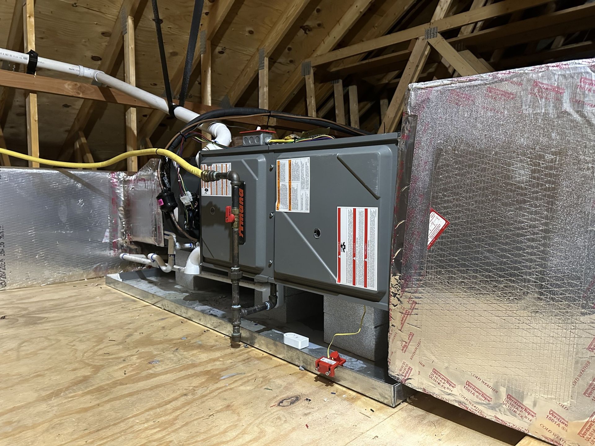 HVAC air handler unit installed in an attic with insulated ductwork and a yellow electrical cable.